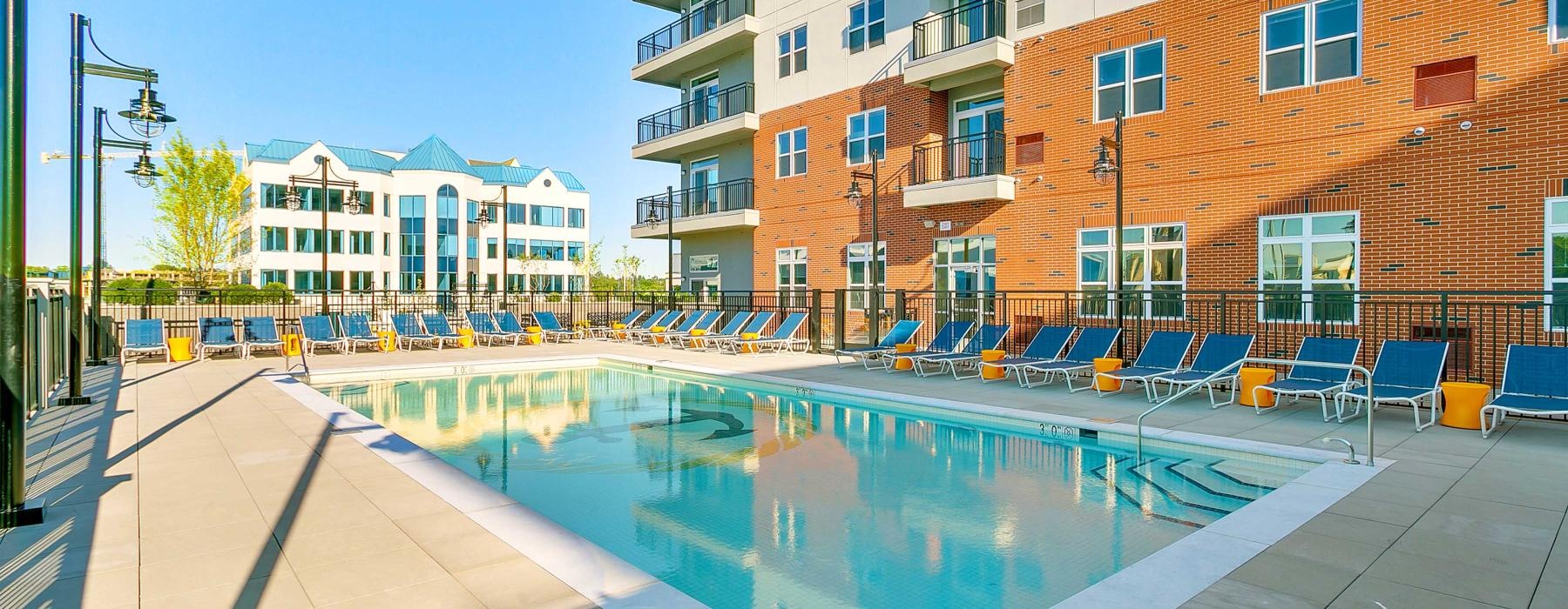 The pool area at our apartments for rent in Stamford, CT, featuring beach chairs and a view of the apartment complex.